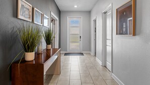 A hallway with a wooden reception desk, potted plants, framed pictures on the wall, and a door at the end. - Spacious Villa w/ Pool, Theater & Game Room (Davenport)
