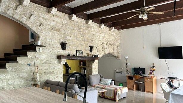 A modern living space with a stone wall, wooden beams, a kitchen area, and a seating area with a sofa and a table. - Villa F3 entre mer et Montpellier (Lattes)