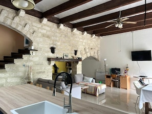 A modern living space with a stone wall, wooden beams, a kitchen area, and a seating area with a sofa and a table. - Villa F3 entre mer et Montpellier (Lattes)