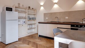 A modern kitchen with a refrigerator, microwave, and stove. There are shelves with glassware and a dining table with chairs.
