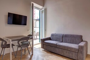Ein modernes Wohnzimmer mit grauem Sofa, einem Esstisch mit Stühlen und einem flachbildfernseher an der Wand.
