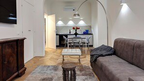 A modern living room with a grey sofa, a wooden cabinet, and a dining area with a table and chairs.