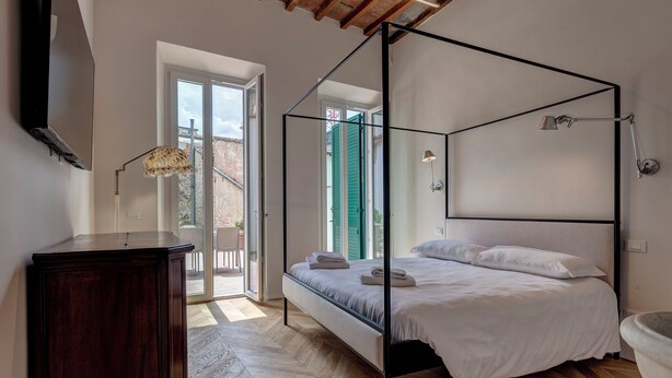 A bedroom with a four-poster bed, a wooden dresser, and a large window with a view of the outside.