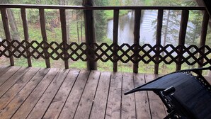 Une terrasse en bois avec une balustrade ajourée donnant sur une zone boisée et un plan d’eau.