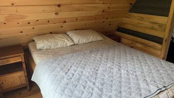 Ein Zimmer einer Holzhütte mit einem Bett, zwei Kissen, einem Nachttisch und einer Holzkommode.
