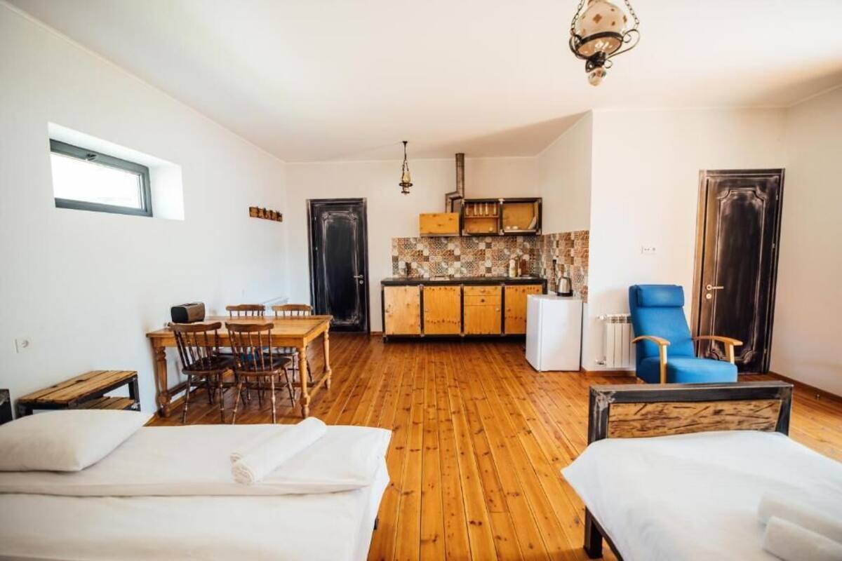 Ein gemütlicher Raum mit Holzboden, einer Essecke mit Stühlen, einem Bett mit Kopfteil, einer Küchenzeile mit Schränken und einem blauen Sessel.
