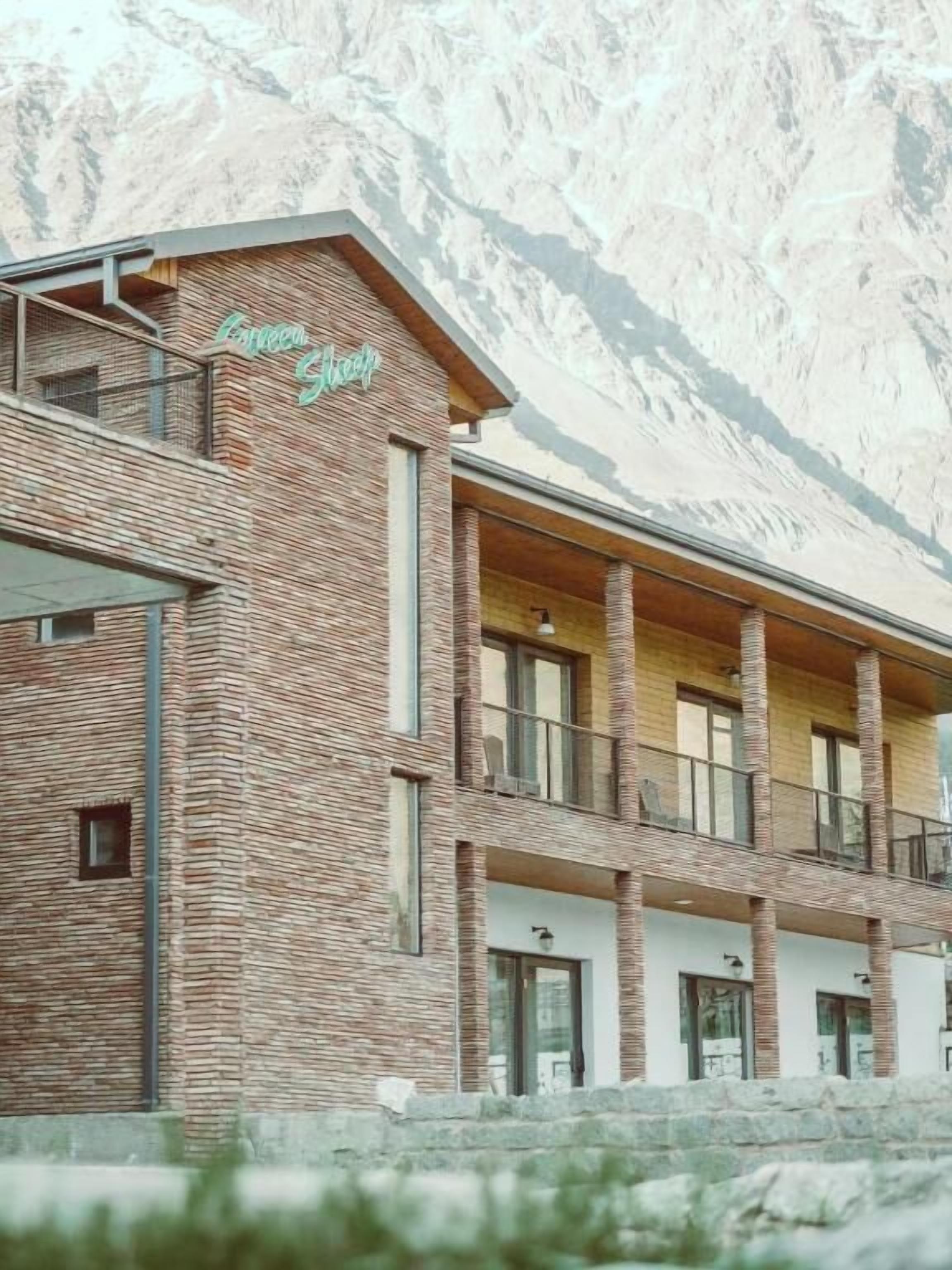Un hotel de varios pisos con fachada de ladrillo, balcones y montañas al fondo.