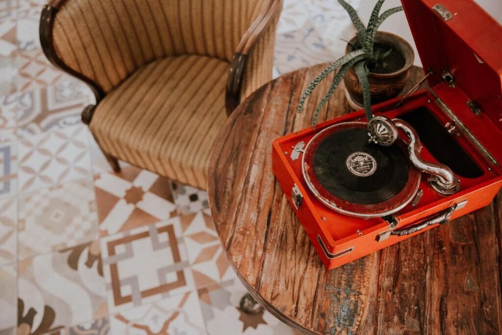 Un vieux gramophone posé sur une table en bois, avec un sol à motifs et une chaise à rayures en arrière-plan.