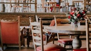 A dining area with wooden chairs and tables, a vase with flowers, and a bookshelf in the background. - Green Sheep Boutique Hotel (Stepantsminda)