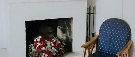 Una habitación con chimenea, un sillón azul con lunares y una estantería con objetos decorativos.