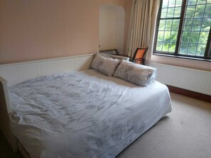 A bedroom with a large bed, a window with curtains, and a radiator. - Charming family home in the heart of Sanderstead. (Greater London)