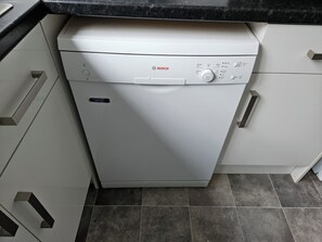 A Bosch dishwasher in a kitchen with white cabinets and a black countertop. - Charming family home in the heart of Sanderstead. (Greater London)