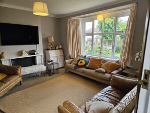 A living room with a sofa, a television, a fireplace, and a window with curtains. - Charming family home in the heart of Sanderstead. (Greater London)