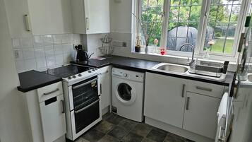 A compact kitchen with white cabinets, a stove, a washing machine, and a window with a view of greenery.