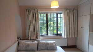 A bedroom with a bed, a window with curtains, a radiator, and a wardrobe. - Charming family home in the heart of Sanderstead. (Greater London)