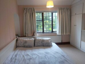 A bedroom with a bed, a window with curtains, a radiator, and a wardrobe. - Charming family home in the heart of Sanderstead. (Greater London)