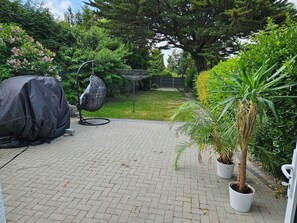 A paved patio with a covered grill, a hanging chair, and potted plants. - Charming family home in the heart of Sanderstead. (Greater London)