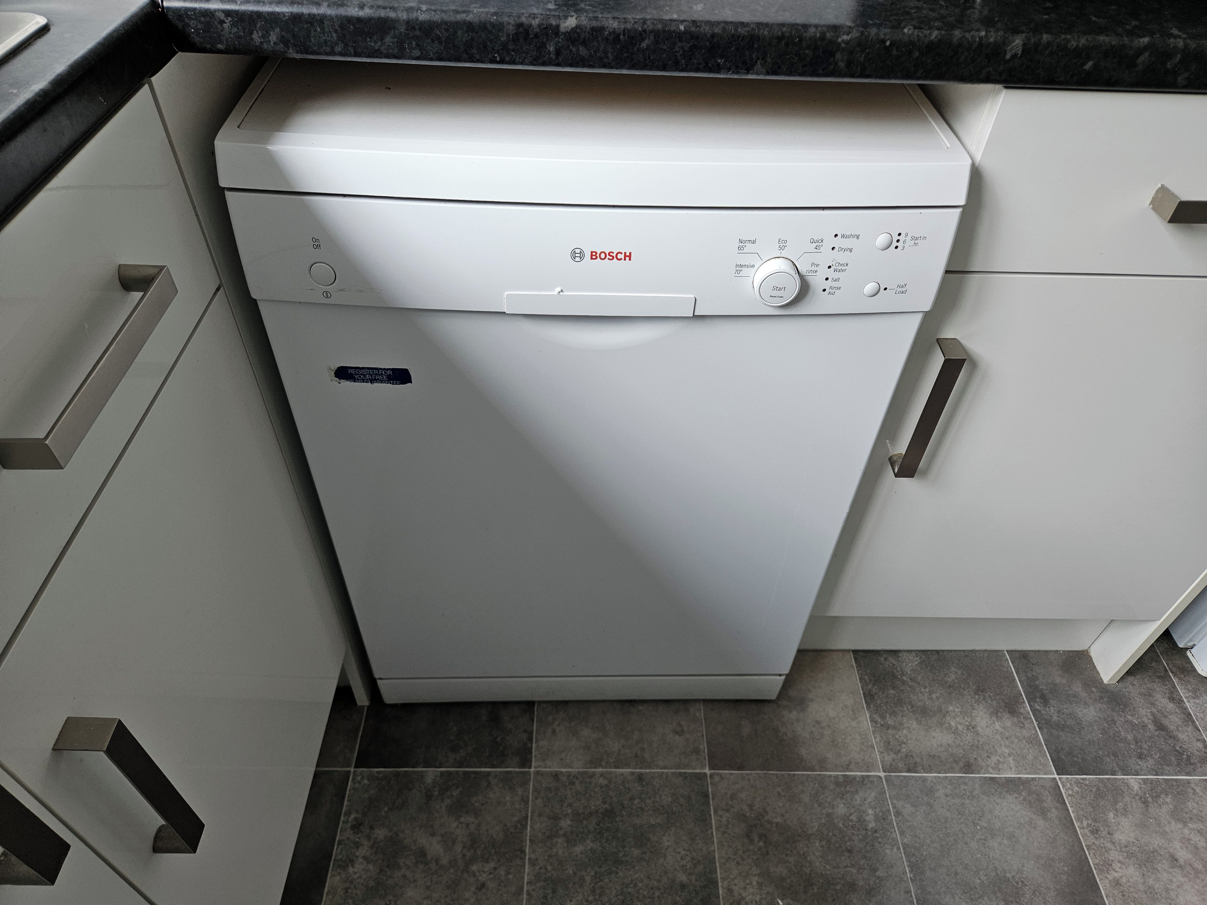 A Bosch dishwasher in a kitchen with white cabinets and a black countertop.