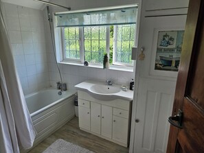 A bathroom with a bathtub, a sink, and a window with a view of greenery. - Charming family home in the heart of Sanderstead. (Greater London)