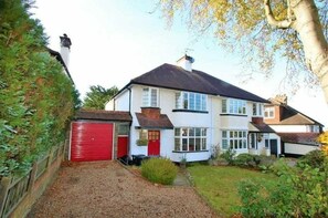 A two-story house with a red garage door, a chimney, and a well-maintained garden. - Charming family home in the heart of Sanderstead. (Greater London)