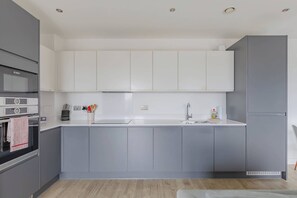 Une cuisine moderne avec des meubles gris, un plan de travail blanc et un four Bosch.