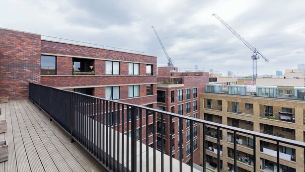 A multi-story building with a brick facade, balconies, and a wooden deck. - Modern Canal-Side 1BD Flat, Heart of Hackney (Greater London)