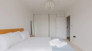 A hotel room with a bed, a wooden headboard, a bedside table, a mirror, a wardrobe, and a bathroom door. - Modern Canal-Side 1BD Flat, Heart of Hackney (Greater London)