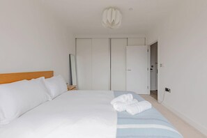 A hotel room with a bed, a wooden headboard, a bedside table, a mirror, a wardrobe, and a bathroom door. - Modern Canal-Side 1BD Flat, Heart of Hackney (Greater London)