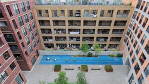 A multi-story building with a central courtyard featuring a swimming pool, surrounded by balconies and greenery. - Modern Canal-Side 1BD Flat, Heart of Hackney (Greater London)