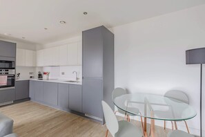 A modern kitchen with grey cabinets, a glass dining table, and a grey sofa.
