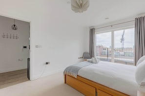 A bedroom with a large bed, a desk, a chair, a window with curtains, and a view of the cityscape.