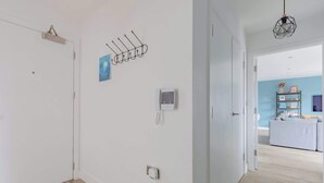 A hallway with a door, a wall-mounted phone, a wall-mounted light fixture, and a door with a geometric-patterned rug.