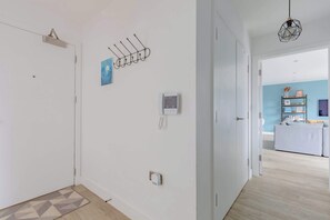A hallway with a door, a wall-mounted phone, a wall-mounted light fixture, and a door with a geometric-patterned rug. - Modern Canal-Side 1BD Flat, Heart of Hackney (Greater London)