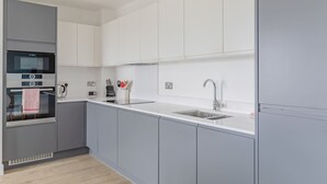 A modern kitchen with grey cabinets, a white countertop, a built-in oven, and a stainless steel sink. - Modern Canal-Side 1BD Flat, Heart of Hackney (Greater London)