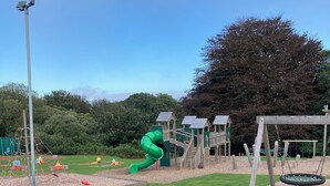 Une aire de jeux avec un toboggan vert, des balançoires et une structure d’escalade.