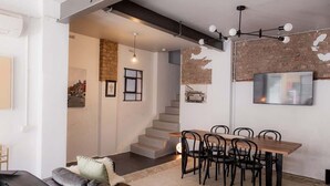A modern living room with a dining area, featuring a staircase, a fireplace, and a large TV mounted on the wall. - Entrepot de Ville (Hobart)