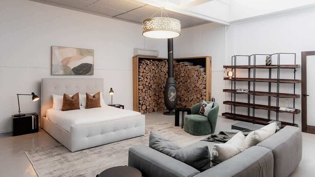 A modern bedroom with a large bed, a green armchair, a grey sofa, a fireplace, and a bookshelf. - Entrepot de Ville (Hobart)