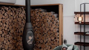 A modern living room with a large, circular, patterned ceiling light, a black wood-burning stove, a stack of firewood, a green armchair, and a white sofa. - Entrepot de Ville (Hobart)