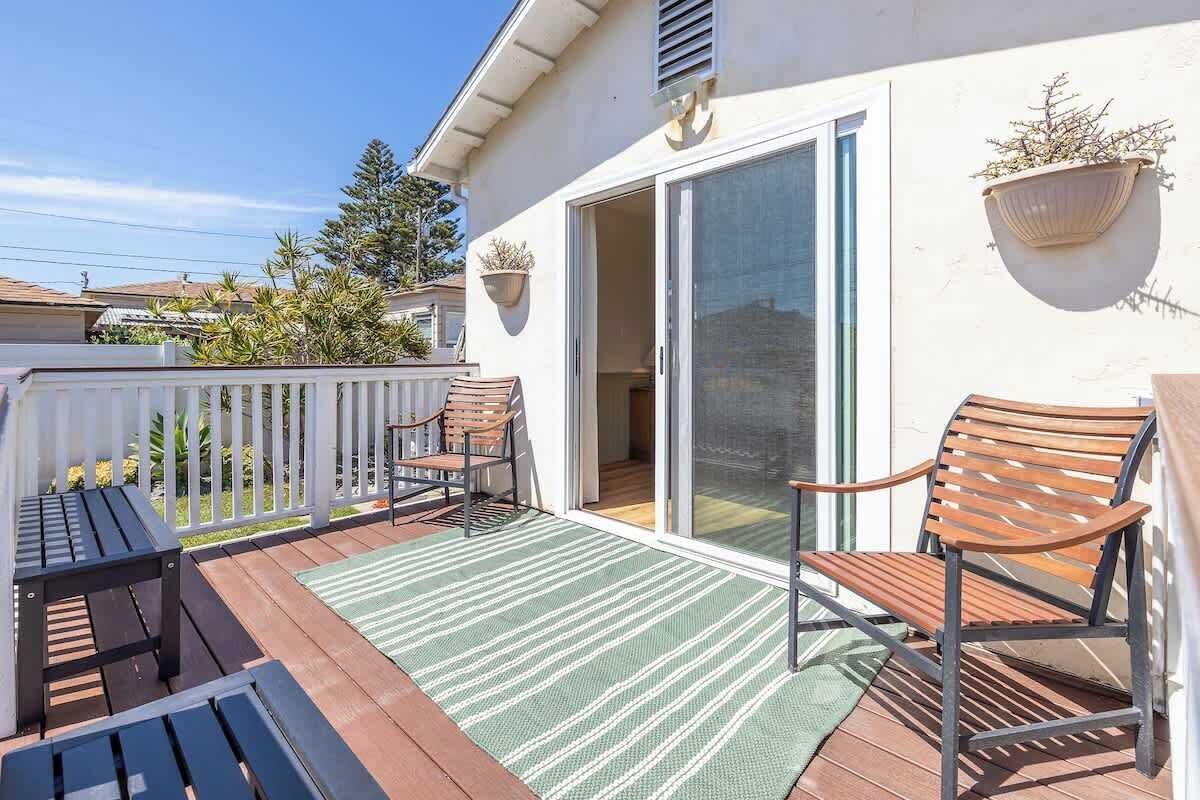 A covered patio with wooden furniture, a sliding glass door, and potted plants.