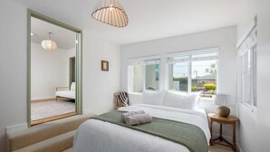 A bedroom with a large bed, a mirror, a window, and a lamp. - Carlsbad Cottage - Remodeled (Carlsbad)