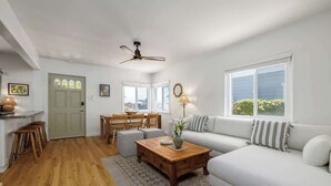 A spacious living room with a white sofa, wooden coffee table, and a dining area with a wooden table and chairs. - Carlsbad Cottage - Remodeled (Carlsbad)