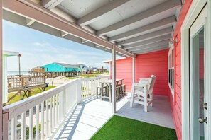 A covered porch with a white railing, a small table and chairs, and a view of the beach and ocean. - The Mermaid Cove Beach House with Ocean Views (Freeport)