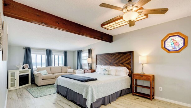 A bedroom with a bed, a sofa, a wooden ceiling fan, and a window with curtains. - The Mermaid Cove Beach House with Ocean Views (Freeport)