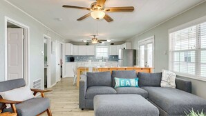 A modern living room with grey sofas, a wooden coffee table, and a ceiling fan. - The Mermaid Cove Beach House with Ocean Views (Freeport)