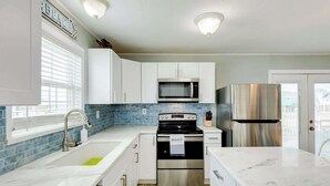 A modern kitchen with white cabinets, a stainless steel refrigerator, a microwave, and a stove. - The Mermaid Cove Beach House with Ocean Views (Freeport)