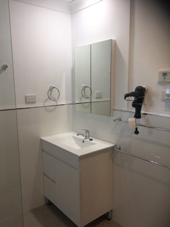 A modern bathroom with a white sink, a mirror, and a hairdryer mounted on the wall.