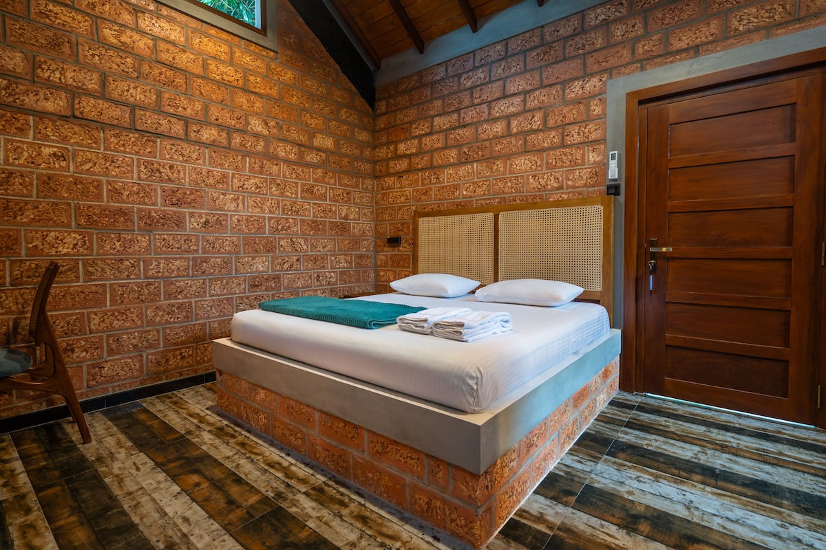 Ein Zimmer mit einer Ziegelwand, einer Holztür, einem Bett mit weißer Bettwäsche und Holzboden.