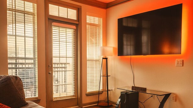 Un salon avec un canapé, un téléviseur fixé au mur et une lampe sur pied.