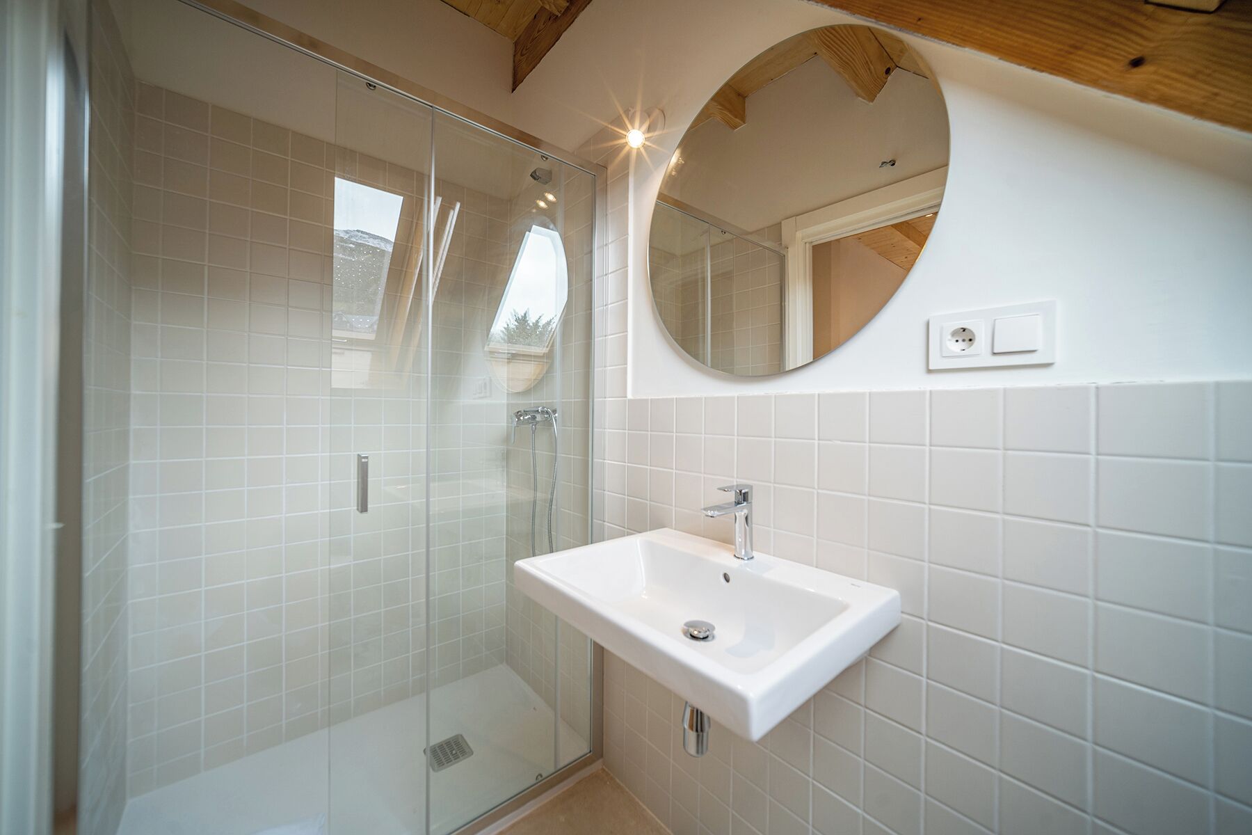 A bathroom with a glass-enclosed shower, a white sink, and a round mirror.