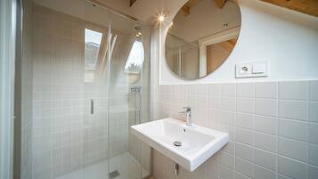 A bathroom with a glass-enclosed shower, a white sink, and a round mirror.